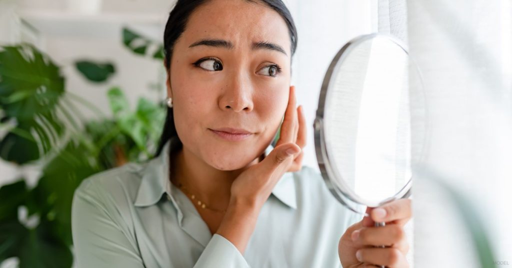 Woman looking in mirror, wondering if she needs BOTOX or dermal fillers (MODEL)